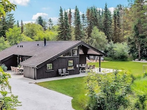 A cabin with a sloped roof, a patio with outdoor seating, and a surrounding forest.