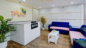 Un espace d’accueil comprenant un comptoir de réception portant l’inscription « OYO », un canapé bleu, une table basse blanche et un ventilateur de plafond.