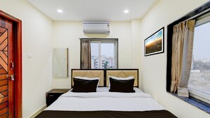 Une chambre d’hôtel comprenant un lit, un climatiseur, une fenêtre avec des rideaux, un tableau encadré au mur et une porte ornée d’un motif géométrique.