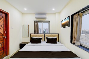 A hotel room with a bed, an air conditioner, a window with curtains, a framed picture on the wall, and a door with a geometric design. - Townhouse Sunnam Cheruvu Lake (Hyderabad)