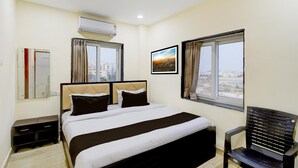 Une chambre d’hôtel avec un lit, une chaise, un appareil de climatisation, une fenêtre avec des rideaux et un tableau encadré au mur.