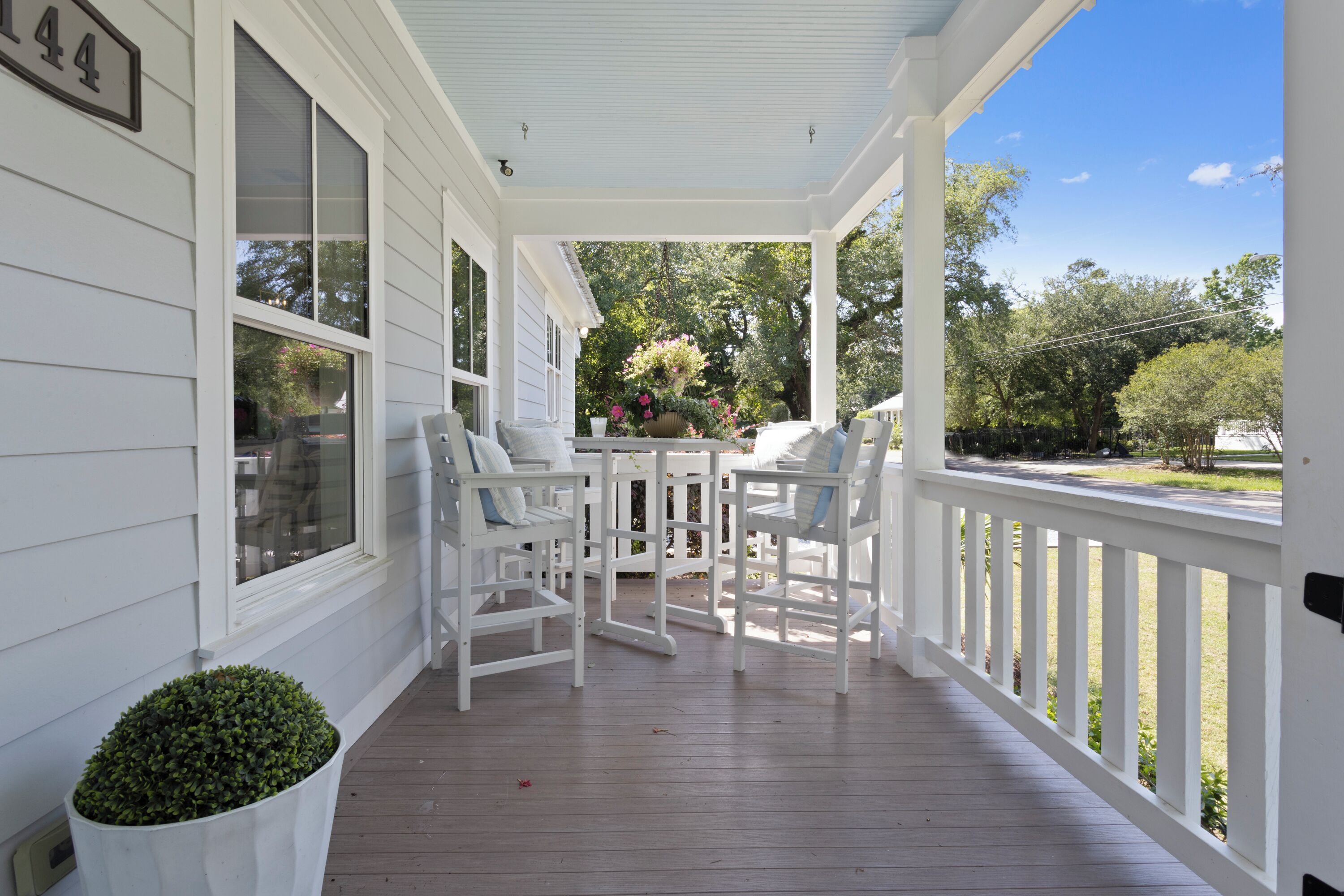 Une véranda avec des balustrades blanches, une table avec des chaises et un pot de fleurs.