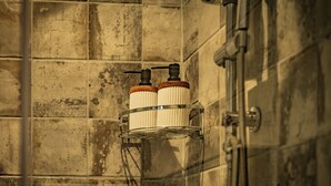 A shower area with tiled walls, a metal shower head, and two soap dispensers mounted on a metal rack.
