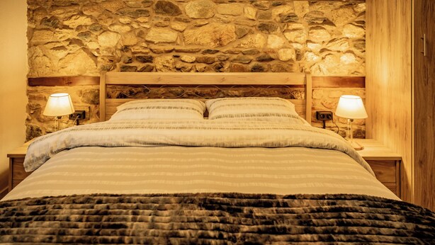 A bed with a stone wall backdrop, two bedside lamps, and a dark throw blanket.
