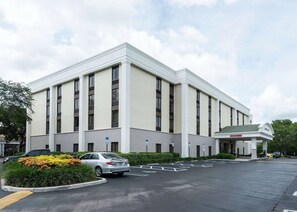 Un grande edificio con tetto piatto, diverse finestre e un parcheggio con posti delimitati.