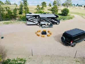 Una caravana con cama cubierta y un vehículo negro estacionado en un área de grava con un cerco perimetral.