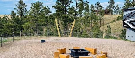 An outdoor area with a gravel ground, a fire pit, and wooden benches arranged in a circle.