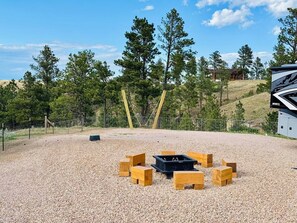 Un espacio al aire libre con suelo de grava, un brasero y bancos de madera dispuestos en círculo.