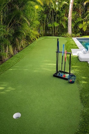 A neatly manicured lawn with a croquet set, a small pool, and lush tropical vegetation. - Heart of Pine Ave | 6 En-Suites | Heated Pool (Anna Maria)