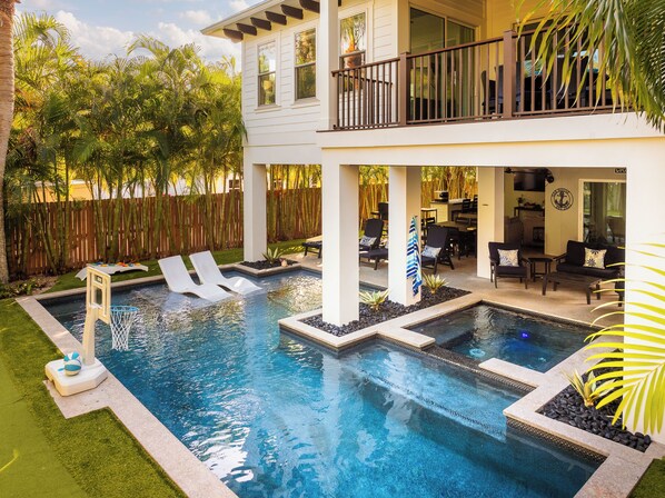 A two-story house with a swimming pool, outdoor furniture, and a wooden fence. - Heart of Pine Ave | 6 En-Suites | Heated Pool (Anna Maria)
