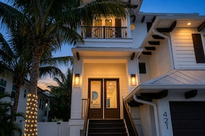A two-story house with a balcony, a front door with a glass panel, and a staircase leading to the entrance. - Heart of Pine Ave | 6 En-Suites | Heated Pool (Anna Maria)