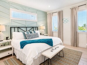 A bedroom with a bed, bedside tables, a bench, a window with curtains, and a wall-mounted light fixture. - Heart of Pine Ave | 6 En-Suites | Heated Pool (Anna Maria)