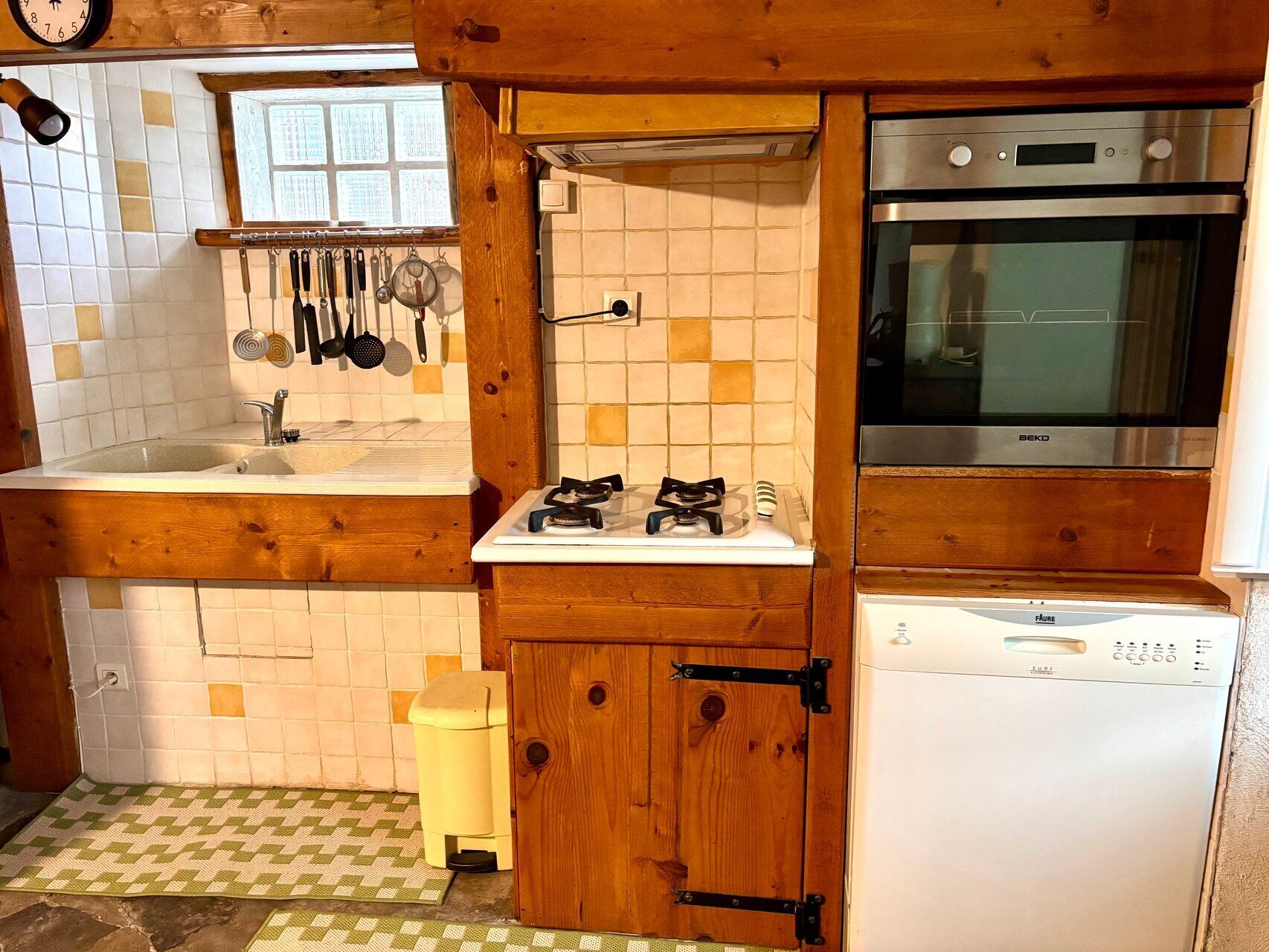 Een keuken met een spoelbak, fornuis, oven en houten kastjes.