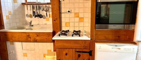 Een keuken met een spoelbak, fornuis, oven en houten kastjes.