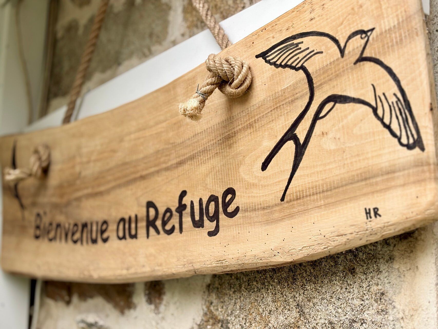 Un letrero de madera con una ilustración de un pájaro y el texto 'Bienvenue au Refuge', señal de bienvenida a un refugio.