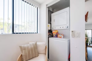 Eine kompakte Küche mit integriertem Waschtrockner, einem Fenster mit Jalousien und einer Couch mit gestreiftem Kissen.