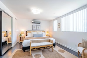 Ein modernes Schlafzimmer mit einem großen Bett, Nachttischen, einer Bank, einem Spiegel und einem Fenster mit Jalousien.