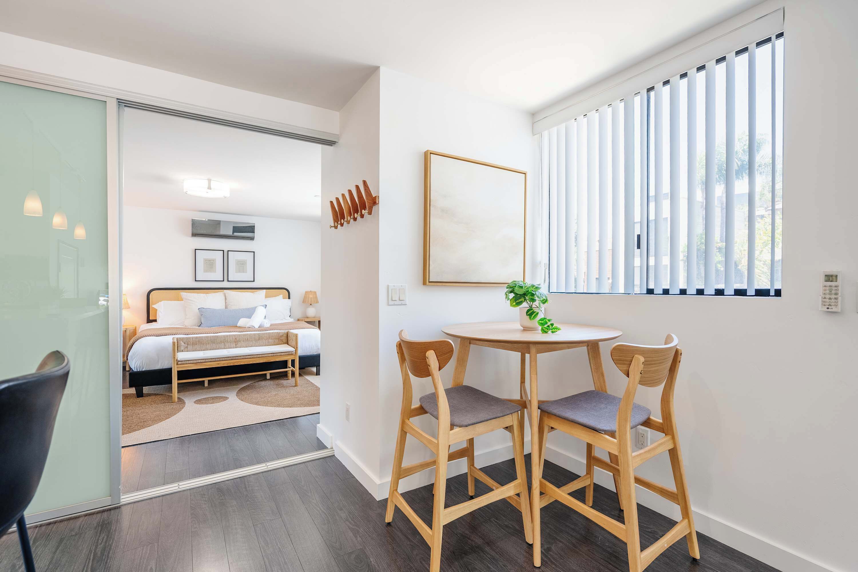 A modern hotel room with a bed, bedside table, chair, and a window with blinds.