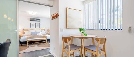 A modern hotel room with a bed, bedside table, chair, and a window with blinds.