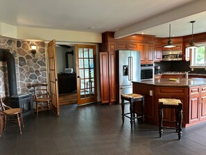Una cocina con pared de piedra, armarios de madera, un refrigerador grande, una estufa y una isla integrada con taburetes.