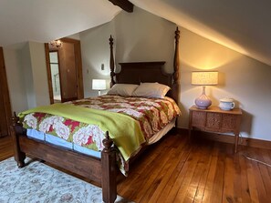 A bedroom with a four-poster bed, a wooden nightstand with a lamp, and a floral-patterned bedspread.