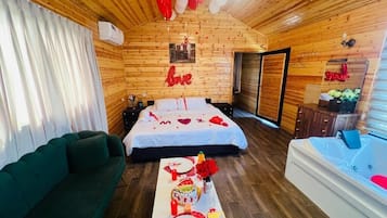 A cozy room with a bed, a green sofa, a dining table with a cake, and a jacuzzi.