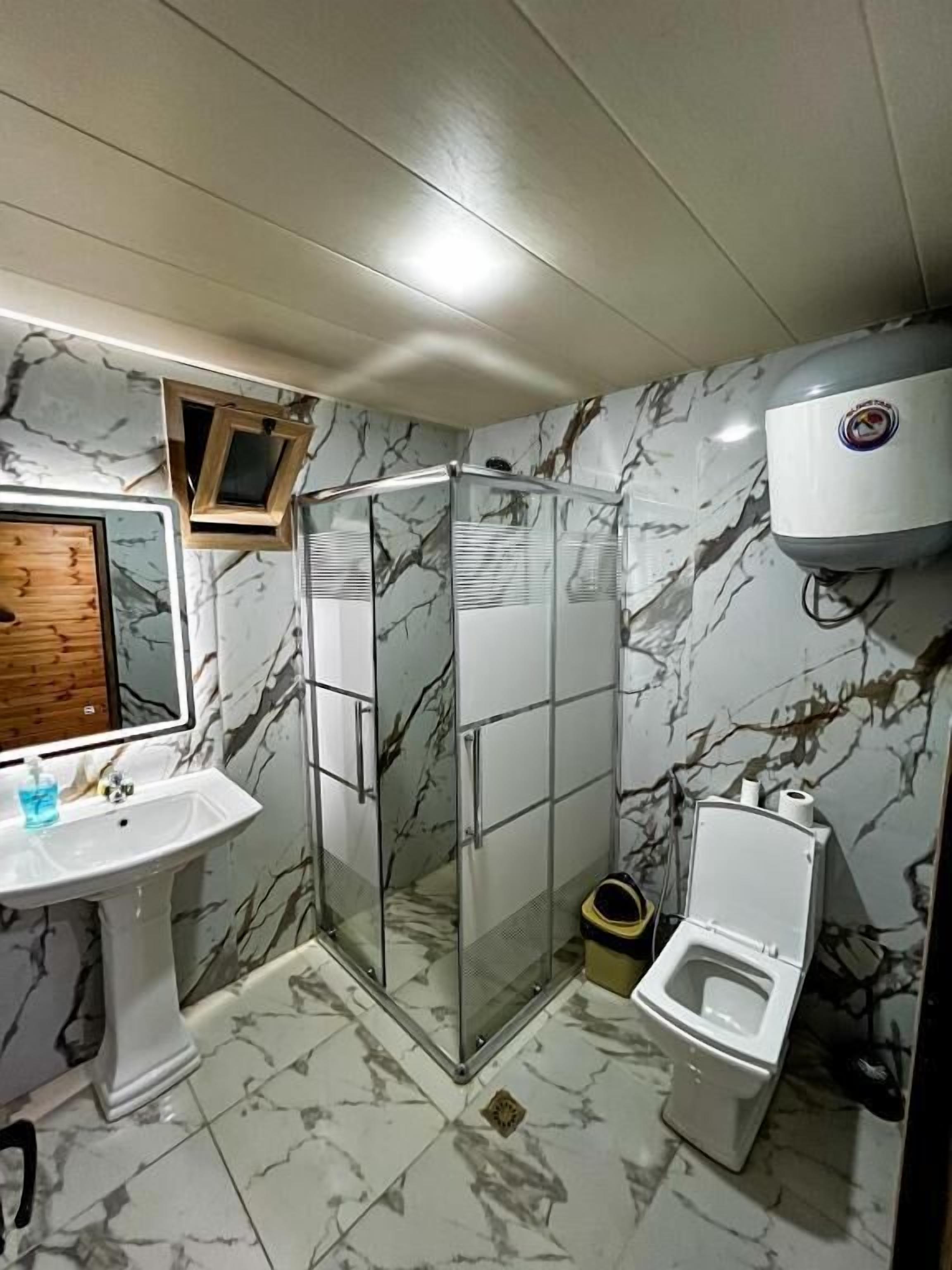 Une salle de bain avec un mur en marbre, une douche en verre, des toilettes et un lavabo.