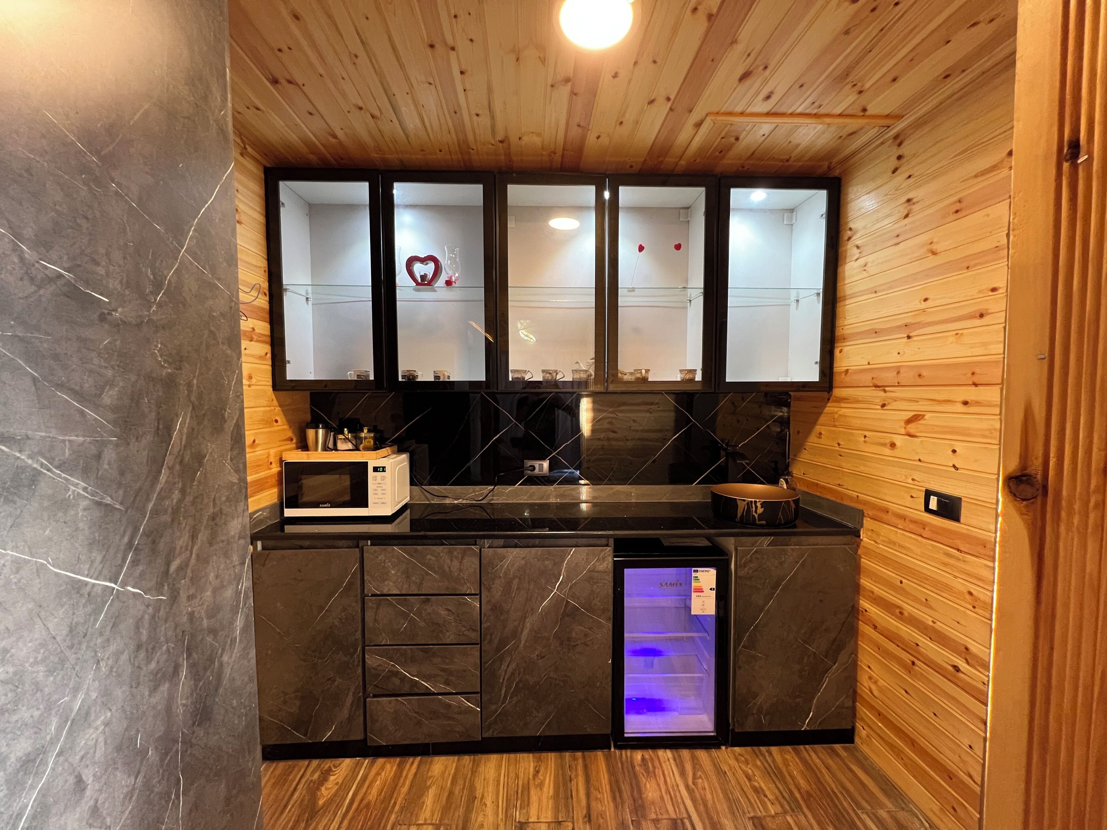Cocina compacta con microondas, pileta y refrigerador, que presenta techo de madera y salpicón de azulejos.