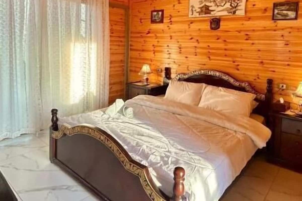 Una habitación con paneles de madera, una cama, una mesita de noche, una lámpara y una silla.