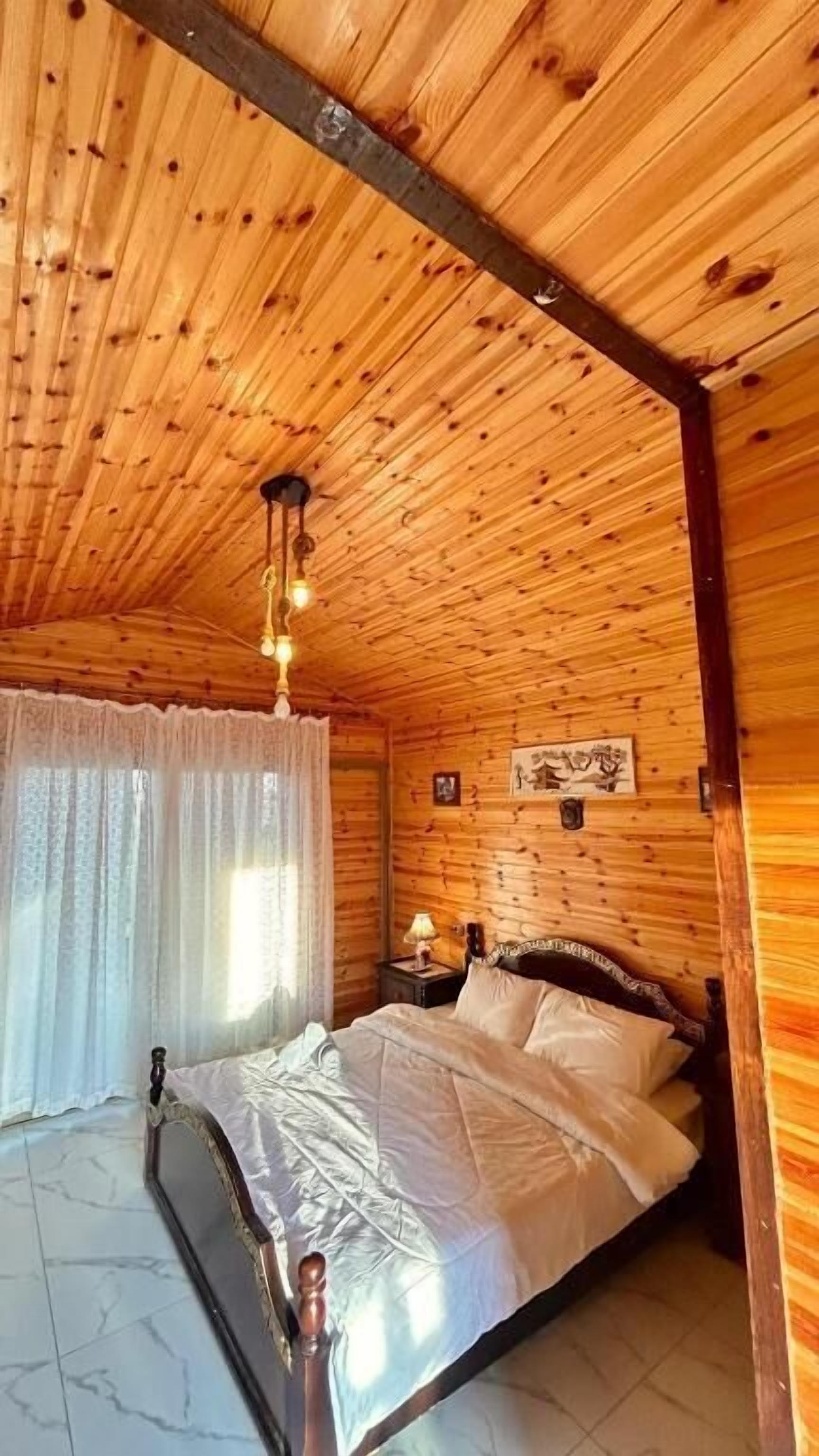A wooden-paneled room with a bed, a nightstand, and a hanging light fixture.