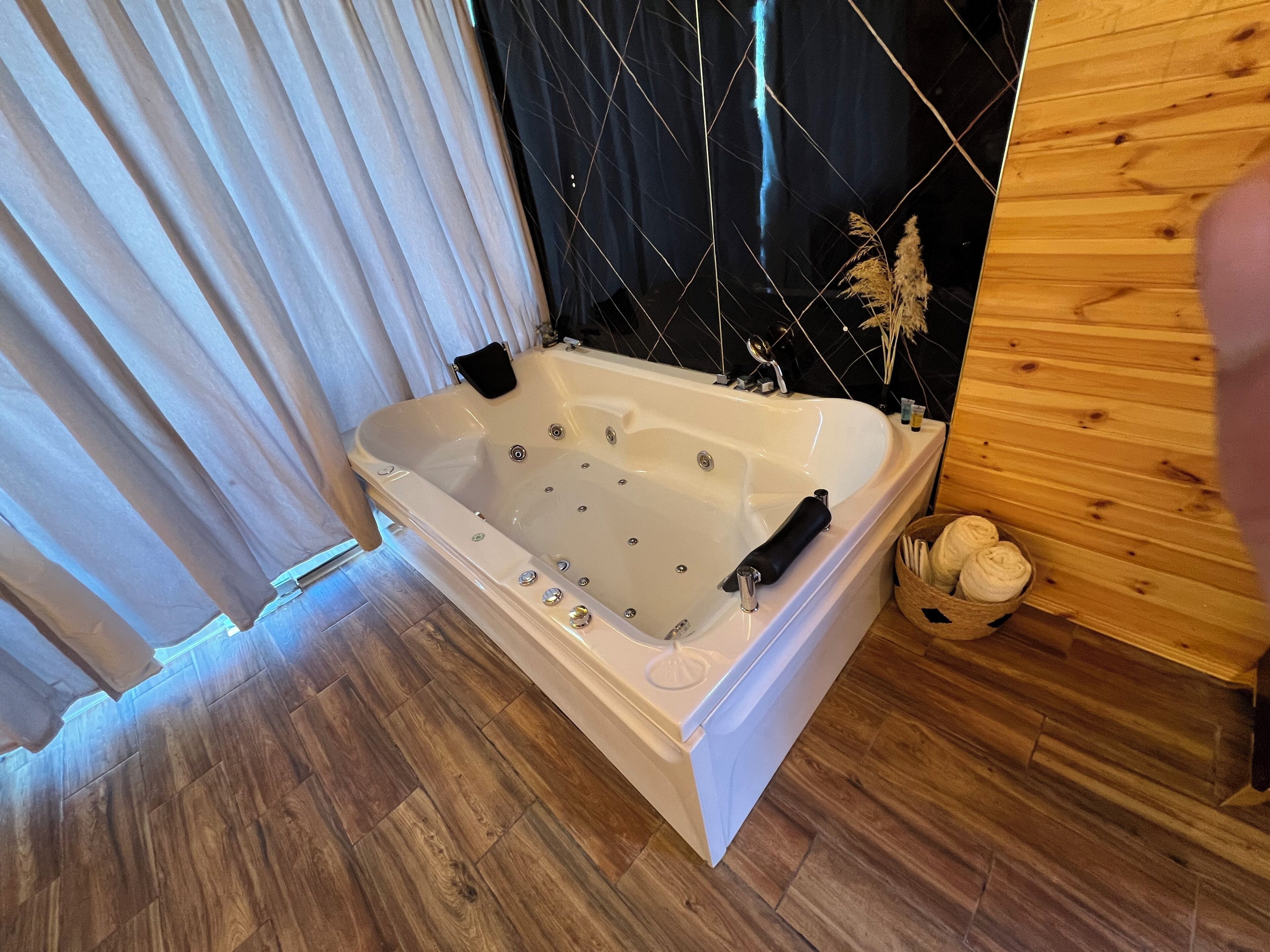 Ein modernes Badezimmer mit freistehender Badewanne, Holzboden und einer schwarzen Wandfliesen.
