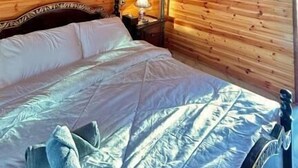 Una habitación con paneles de madera, una cama, un aire acondicionado de pared, una lámpara y un cuadro enmarcado.
