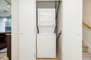 Ein kleiner Waschraum mit Waschmaschine und Trockner, einer Holztreppe und Blick zum Küchenbereich.