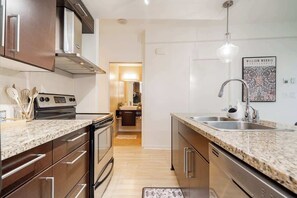 Een moderne keuken met roestvrijstalen apparatuur, granieten aanrecht en uitzicht op de eetruimte.