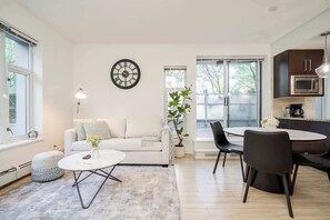 Een moderne woonkamer met een witte bank, een ronde salontafel, een eethoek met een tafel en stoelen, een klok aan de muur en een potplant.
