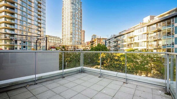 Terraço no telhado com guarda-corrimão de metal, céu claro e edifícios altos ao redor.