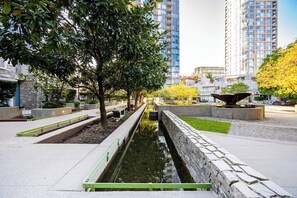 Een aangelegde stedelijke omgeving met een waterpartij, banken en hoge gebouwen op de achtergrond.