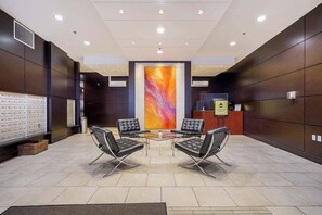 Een lobby met een receptiebalie, twee zwarte leren stoelen, een glazen tafel, een groot abstract schilderij en een inbouwkluis.