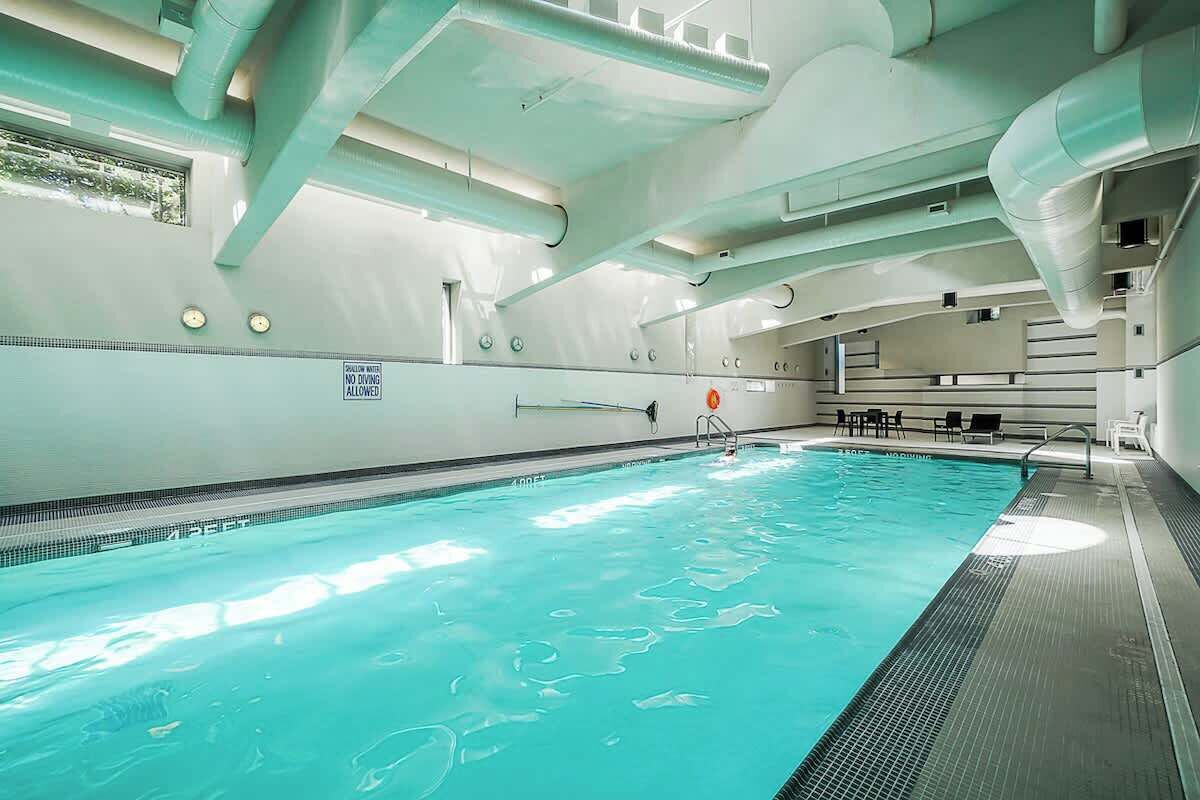 An indoor swimming pool with clear water, a no diving sign, and a sunlit ceiling.