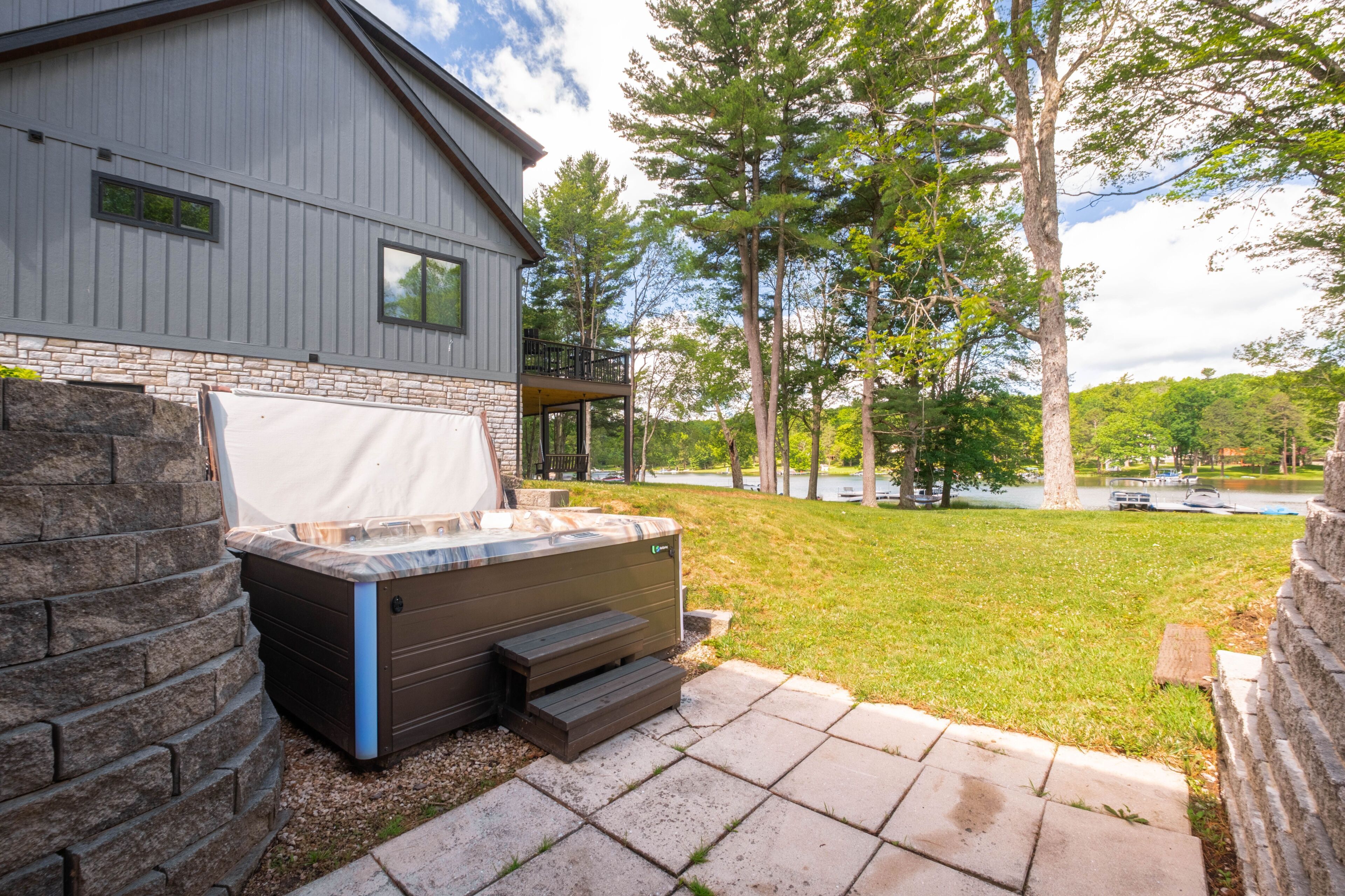 Une maison moderne dotée d’un jacuzzi, d’un escalier en pierre et offrant une vue sur un lac.