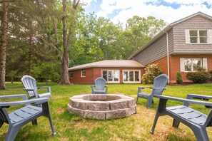 A backyard with a fire pit, outdoor chairs, and a brick house.