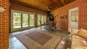 A covered patio area with brick walls, a ceiling fan, a dining table with chairs, and a sofa.