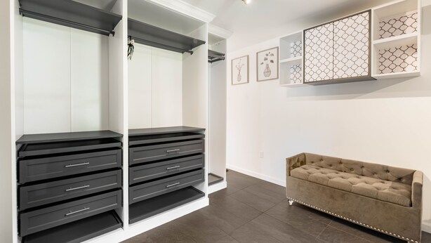 Une pièce avec une armoire blanche, des tiroirs noirs, un canapé beige et des étagères murales ornées d’objets décoratifs.