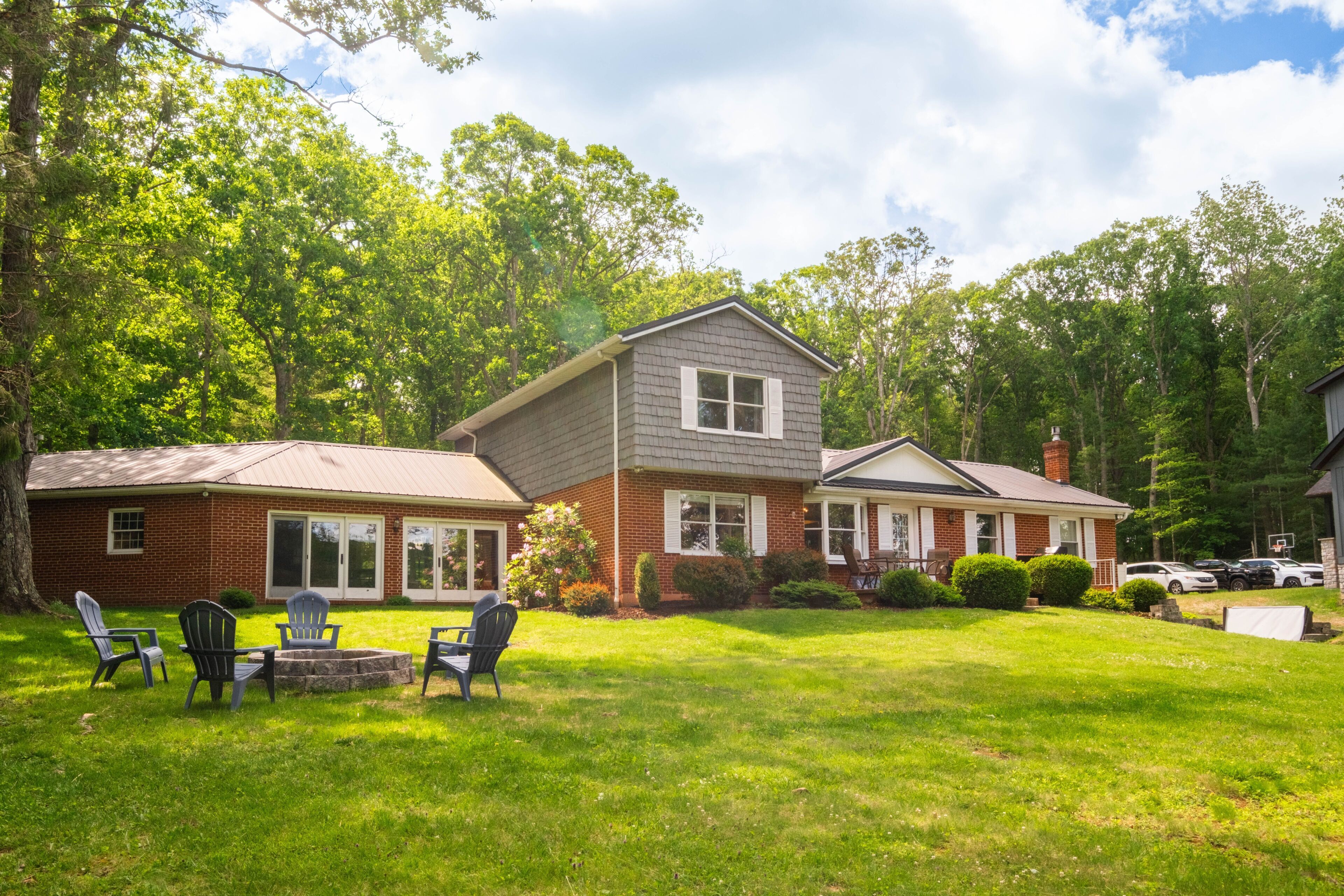 A two-story house with a brick exterior, a front porch, and a backyard with a fire pit and outdoor seating.