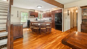 Une cuisine avec un plancher en bois, un îlot central doté de chaises, des armoires en bois et un réfrigérateur.