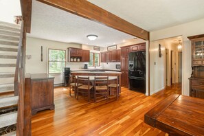 A kitchen with wooden flooring, a central island with chairs, wooden cabinets, and a refrigerator.
