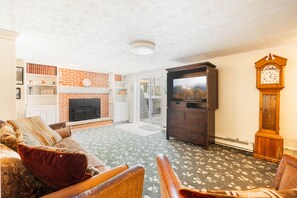A living room with a fireplace, a television, a clock, and a sofa. - Lakefront w Private Dock, Hot Tub, Large Yard (Swanton)
