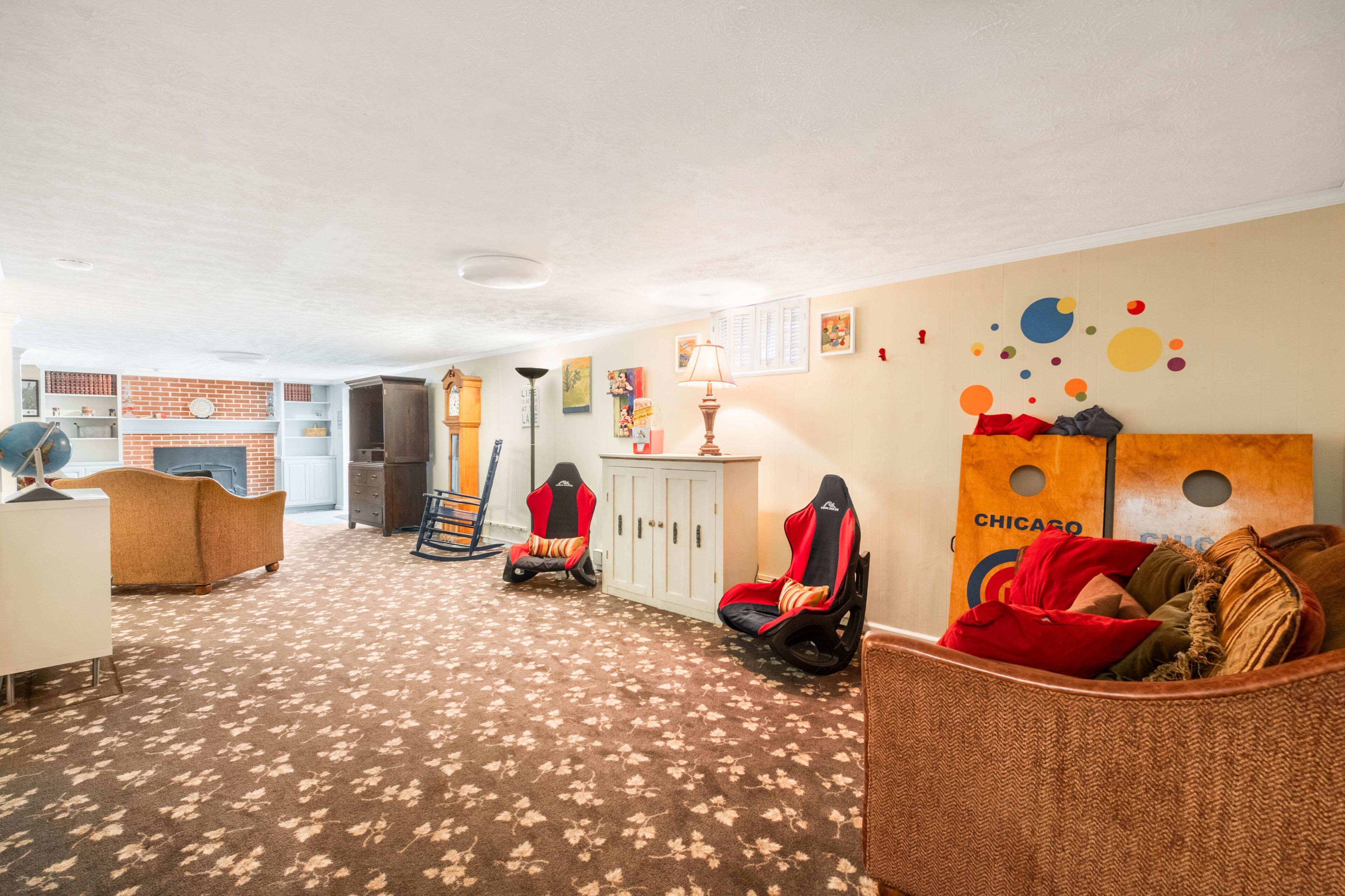 A room with a carpeted floor, a sofa, a gaming chair, a cabinet, and a wall with colorful circular decorations.