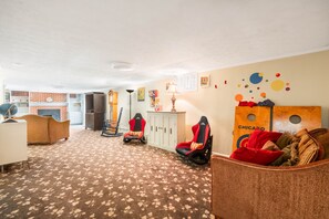 Una habitación con piso alfombrado, un sofá, una silla gamer, un armario y una pared decorada con círculos de colores.