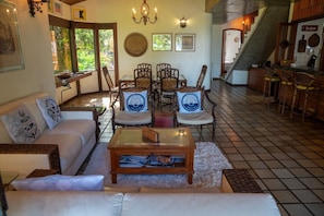 Ein gemütliches Wohnzimmer mit einer Couch, Sesseln, einem Couchtisch und einer Treppe, die in einen Küchenbereich führt.